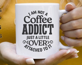May include: White ceramic coffee mug with black text that reads "I am not a coffee addict, just a little over attached to it".