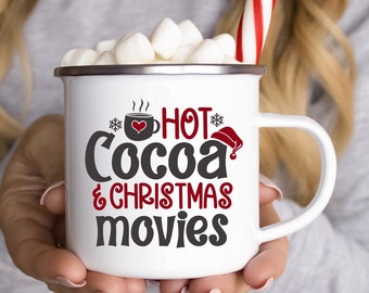 Könnte beinhalten: Eine weiße Tasse mit einem roten Herzen und dem Text "Hot Cocoa & Christmas Movies" in schwarzer und roter Schrift. Die Tasse ist mit Marshmallows gefüllt und im Hintergrund befindet sich ein Zuckerstangen.