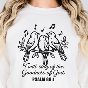 May include: White sweatshirt featuring a black illustration of three birds perched on a branch, with musical notes above. The text reads "I will sing of the Goodness of God, PSALM 89:1". The design is labeled "DIGITAL DESIGN".