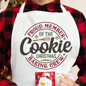 Könnte beinhalten: Eine weiße Schürze mit einem roten, grünen und goldenen Kreisdesign, auf dem "Proud Member of the Cookie Christmas Baking Crew" steht.