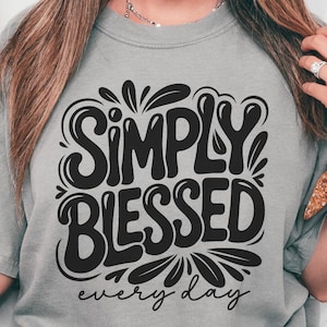 May include: Gray t-shirt with the words "SIMPLY BLESSED" in a bold, black, retro font, with the words "every day" below. The shirt is a casual style, suitable for everyday wear.