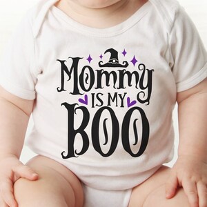 May include: A white baby onesie with black text that reads "Mommy is my Boo" with a purple witch hat and stars above the text.