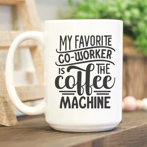 May include: White ceramic coffee mug with the text "MY FAVORITE CO-WORKER IS THE COFFEE MACHINE" in black. The mug has a large handle and is on a wooden surface. The image also includes SVG, DXG, PNG, and EPS file type icons.