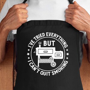 May include: Black apron with a white circle design featuring a smoker grill and the text "I've tried everything but I can't quit smoking".