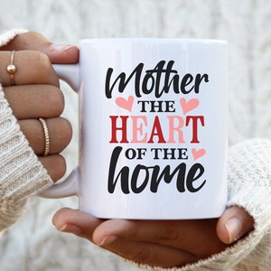 May include: White ceramic mug with black text that reads "Mother the heart of the home" with pink hearts.