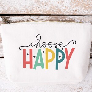 May include: A white canvas zippered pouch with the text "choose happy" in black and colorful letters. The letters are outlined in black and have a sparkly effect. The text is centered on the pouch.