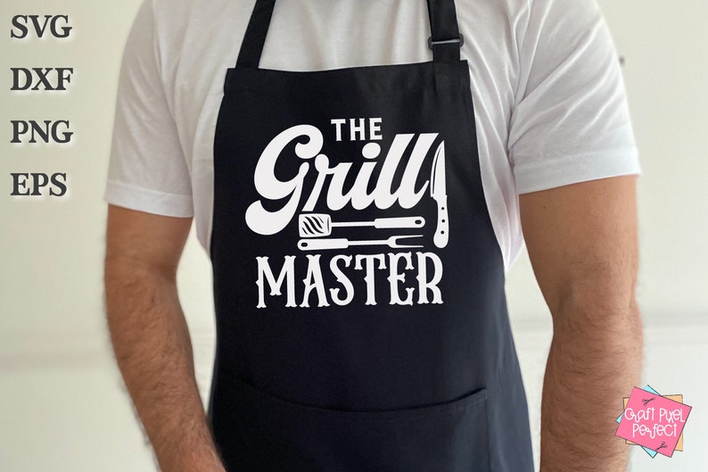 May include: Black apron with a white graphic that reads "THE Grill MASTER" with images of grilling tools. The apron has a front pocket and adjustable neck strap. The apron is worn over a white t-shirt.