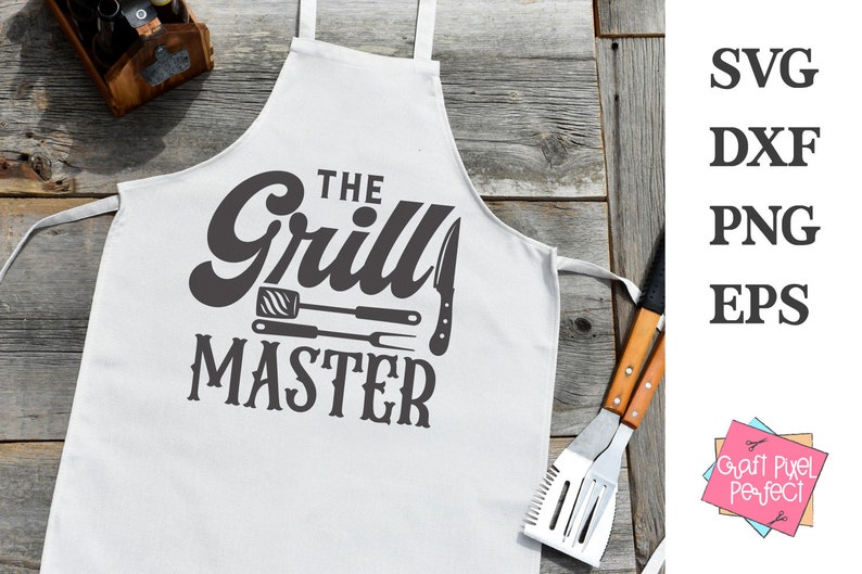 May include: White apron with the text "The Grill Master" in a bold, dark gray font. The design includes illustrations of grilling tools. The apron is displayed on a rustic wooden surface, with grilling utensils and a wooden caddy in the background.