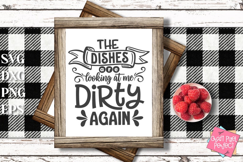 May include: A framed sign with the text "THE DISHES are looking at me DIRTY AGAIN" in black lettering. The sign is set against a black and white checkered background, with a small bowl of raspberries on the right.