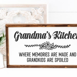 May include: A wooden sign with the text "Grandma's Kitchen" in black cursive font. Below the text is a floral design and the text "Where memories are made and grandkids are spoiled."
