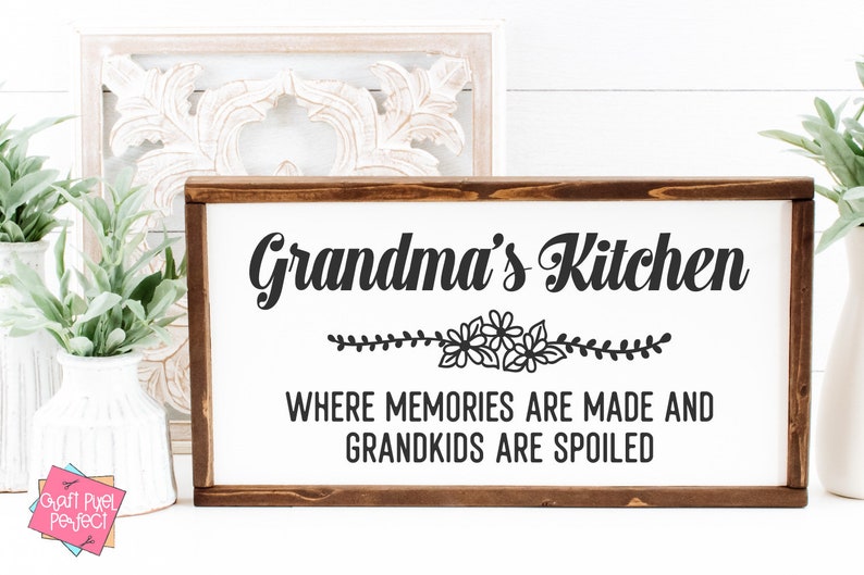 May include: A wooden sign with the text "Grandma's Kitchen" in black cursive font. Below the text is a floral design and the text "Where memories are made and grandkids are spoiled."