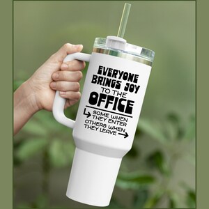 Puede incluir: Taza de viaje blanca con asa negra y una inscripci&oacute;n negra que dice "Todo el mundo trae alegr&iacute;a a la oficina. Algunos cuando entran, otros cuando se van."