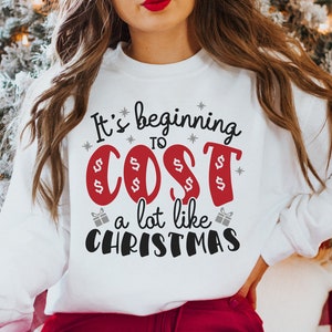 May include: White sweatshirt with a red and black graphic that says "It's beginning to cost a lot like Christmas".