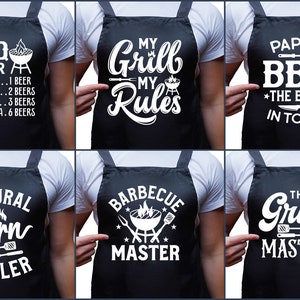 May include: Six different aprons with humorous grilling-themed text printed in white on a black background. The aprons feature sayings like "BBQ Timer", "My Grill My Rules", "Papa's BBQ The Best in Town", "Natural Born Griller", "Barbecue Master", and "The Grill Master".