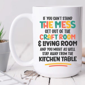 May include: White ceramic mug with a colorful design that reads "If you can't stand the mess get out of the craft room & living room and you might as well stay away from the kitchen table".