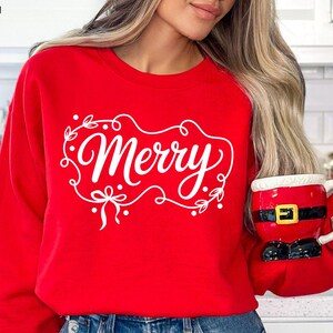 May include: A red sweatshirt with the word "Merry" in white script, framed by a decorative wreath. The person is holding a Santa-themed mug. The image also includes the text "DIGITAL DESIGN" and SVG, PNG, DXF, and EPS file type indicators.