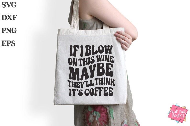 Op de afbeelding: Een witte tote bag met zwarte tekst die "Als ik op deze wijn blaas, denken ze misschien dat het koffie is" zegt.