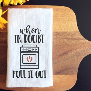 May include: White kitchen towel with black text that reads "when in doubt pull it out" and a black and white illustration of a stove with a brown flame inside.