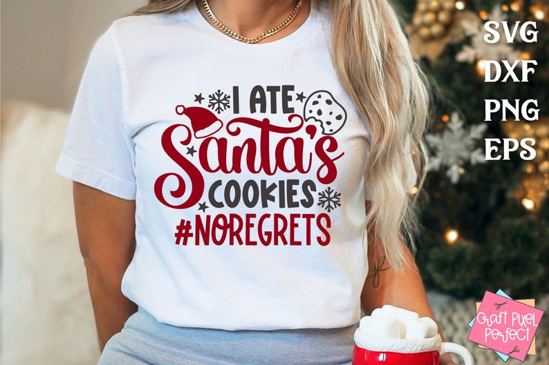 May include: A white t-shirt with the text "I ate Santa's cookies #noregrets" in red and gray lettering. A red Santa hat and a chocolate chip cookie are also included in the design.