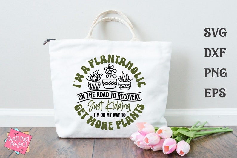 May include: A white tote bag with a green circle design that says "I'm a Plantanholic on the road to recovery. Just kidding, I'm on my way to get more plants." There are three potted plants inside the circle.