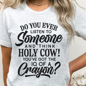 Może przedstawiać: Biała koszulka z czarnym nadrukiem: "Do you ever listen to someone and think HOLY COW! You've got the IQ of a Crayon?"