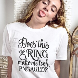 May include: White t-shirt with black text that reads "Does this ring make me look engaged?" with a diamond ring graphic.