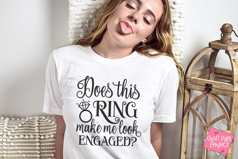 May include: White t-shirt with black text that reads "Does this ring make me look engaged?" with a diamond ring graphic.