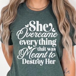 May include: A green t-shirt with the text "She overcame everything that was meant to destroy her" in white lettering with hearts.