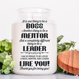 Op de afbeelding: Een witte kaars pot met een zwart tekstontwerp dat "It is one thing to be a BOSS. Another thing to be a MENTOR. But a completely different thing to be a LEADER. I am so proud to be led by a BOSS, MENTOR, and LEADER LIKE YOU! Thank you for being you!" zegt.