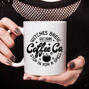 以下が含まれることがあります： 「Witches Brew Coffee Co. Est. 1586 Stop in for a Spell」と書いてある白黒のグラフィックデザインが施された白いコーヒーカップです。