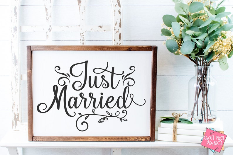 May include: A white wooden sign with a brown frame, featuring the text "Just Married" in a decorative script font with floral embellishments.
