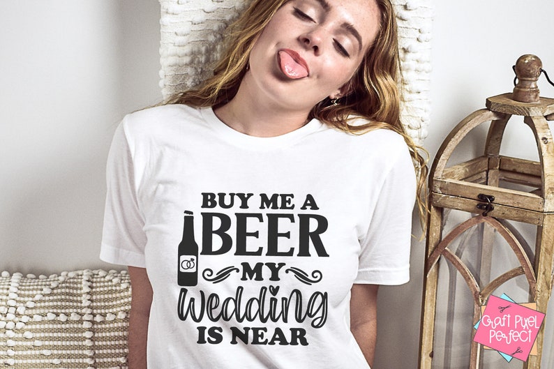 May include: White t-shirt with black text that reads "Buy me a beer my wedding is near". The text is stylized with a beer bottle graphic and wedding rings.