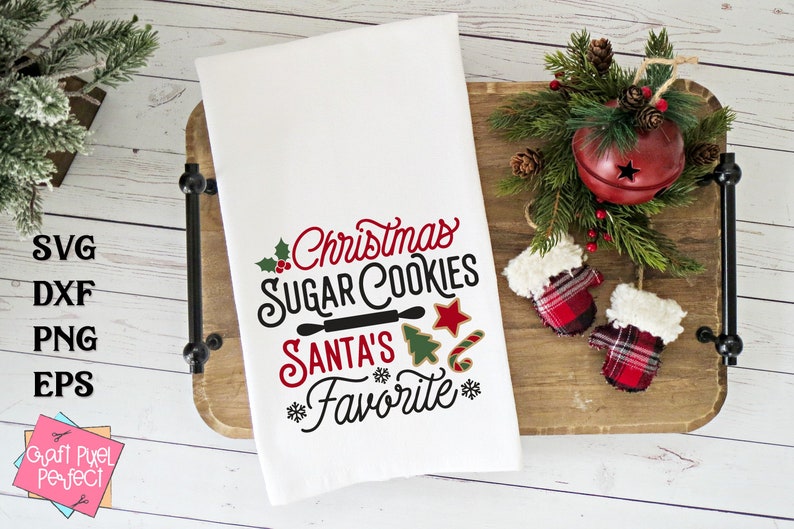 May include: White kitchen towel with the text "Christmas Sugar Cookies Santa's Favorite" in red and black lettering. The text is surrounded by a holly sprig, a rolling pin, a star, a candy cane, and a Christmas tree.