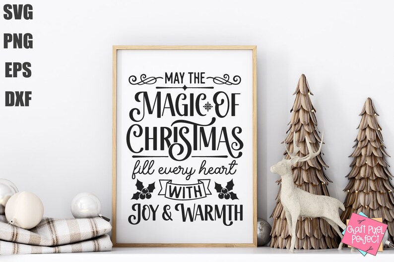 Puede incluir: Una impresi&oacute;n enmarcada blanca con texto negro que dice "Que la magia de la Navidad llene cada coraz&oacute;n de alegr&iacute;a y calidez". La impresi&oacute;n se muestra en un estante blanco con dos &aacute;rboles decorativos y una figura de ciervo.