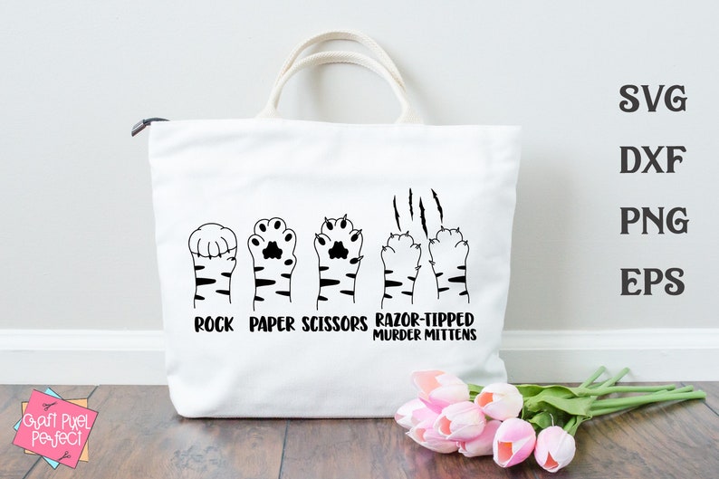 May include: A white tote bag with a black design of five cat paws. The paws are labeled "rock", "paper", "scissors", "razor-tipped", and "murder mittens".