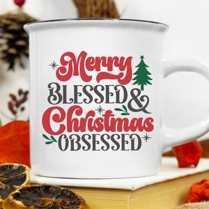 May include: White ceramic mug with a black rim and handle. The mug has a red and black design that says "Merry Blessed & Christmas Obsessed" with a small green Christmas tree graphic.