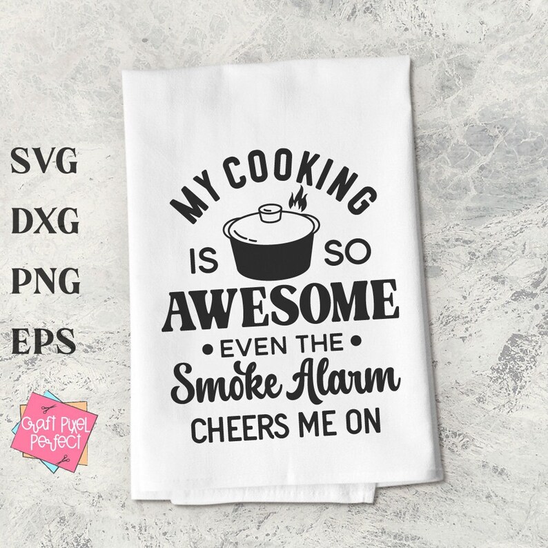 May include: A white kitchen towel with black text that reads "My cooking is so awesome even the smoke alarm cheers me on". The text is surrounded by a black illustration of a pot with a lid.