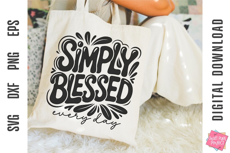 May include: Cream-colored tote bag with the words "SIMPLY BLESSED" in a bold, black, stylized font. Below the main text, the phrase "every day" is written in a smaller, cursive font. The bag is held by a person.