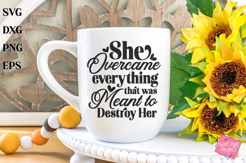 May include: White ceramic mug with a black graphic that reads "She Overcame everything that was Meant to Destroy Her". The mug is sitting on a white pedestal with a string of beads in the foreground.