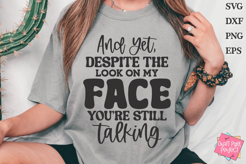 May include: A gray t-shirt with the text "And yet, DESPITE THE LOOK ON MY FACE YOU'RE STILL talking" printed in black.