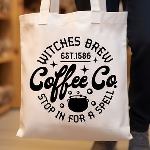 以下が含まれることがあります： 「Witches Brew Coffee Co. Est. 1586 Stop in for a Spell」と書いてある白地に黒と白のデザインのトートバッグ。デザインには、蒸気が出ている釜が描かれている。