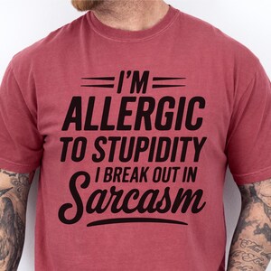 May include: A red t-shirt with the text "I'M ALLERGIC TO STUPIDITY I BREAK OUT IN Sarcasm" printed in black.