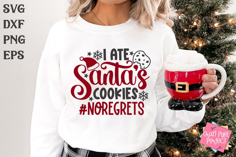 May include: White sweatshirt with red and black text that reads "I ate Santa's cookies #noregrets". The text is surrounded by snowflakes and a red Santa hat. A person is wearing the sweatshirt and holding a red and black Santa mug.