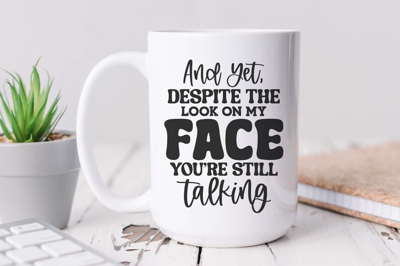 May include: White ceramic coffee mug with black text that reads "And yet, despite the look on my FACE you're still talking".