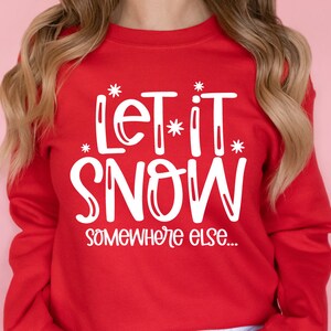 May include: Red sweatshirt with white text that says "Let it snow somewhere else..."
