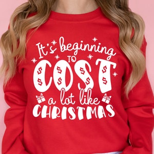 May include: Red sweatshirt with white text that reads "It's beginning to cost a lot like Christmas". The text is surrounded by stars and dollar signs.