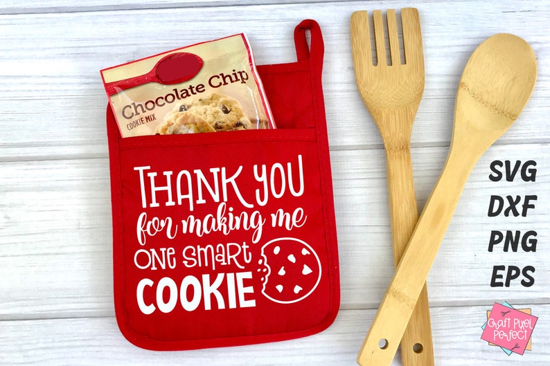 May include: Red oven mitt with a white pocket and the text "THANK YOU for making me ONE SMART COOKIE" with a cookie graphic.  The oven mitt is on a white wood surface with a bag of chocolate chip cookie mix and two wooden kitchen utensils.