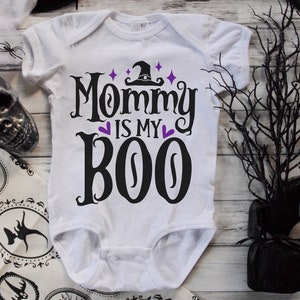 May include: White baby onesie with black text that reads "Mommy is my Boo" with a witch hat and purple hearts.
