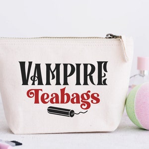 May include: A white canvas zippered pouch with the text "Vampire Teabags" in black and red lettering. A black and red tampon is pictured below the text.