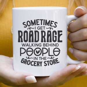 K&ouml;nnte beinhalten: Wei&szlig;e Keramiktasse mit schwarzem Text, der "Sometimes I get road rage walking behind people in the grocery store" lautet.